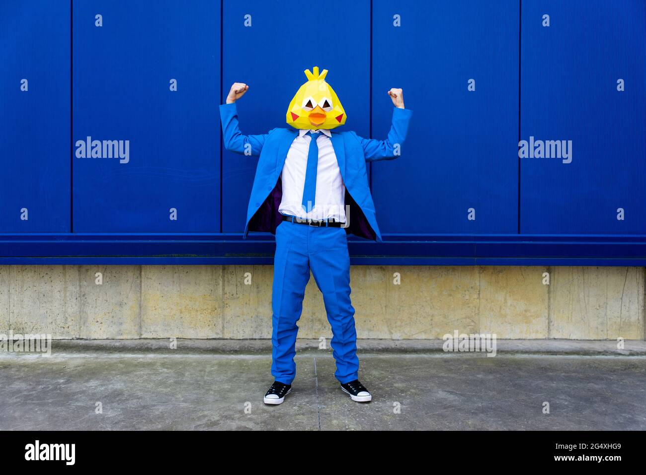 Man wearing vibrant blue suit and bird mask flexing muscles in front of