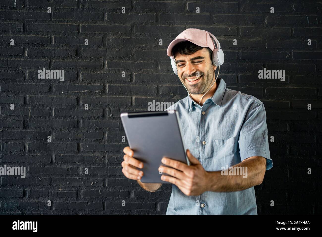 Happy young man using digital tablet in front of wall Stock Photo