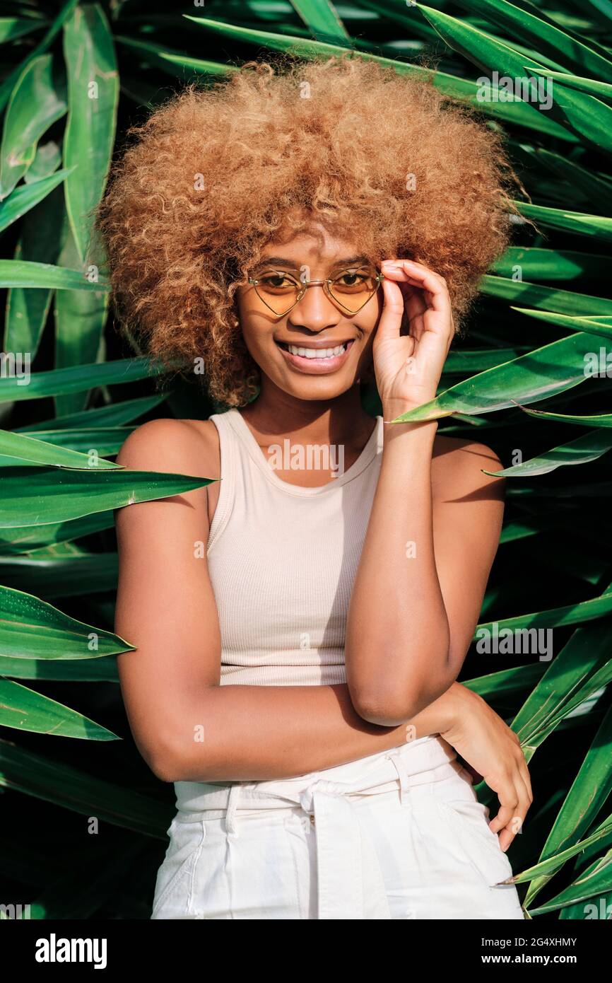 Smiling Young Woman Wearing Sunglasses Standing Amidst Leaves Stock