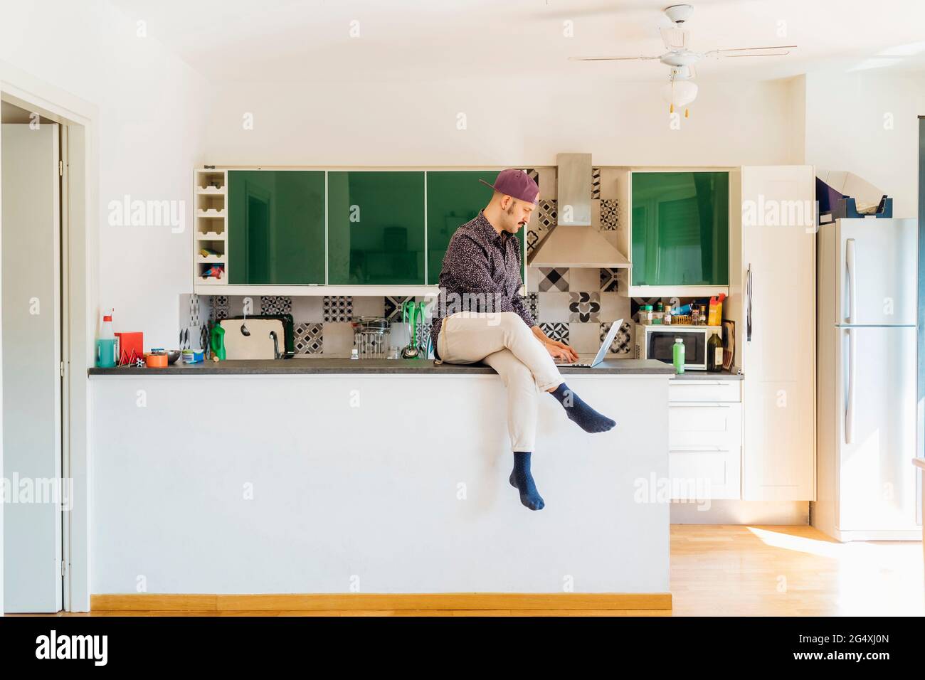Man using laptop while sitting on kitchen island at home Stock Photo