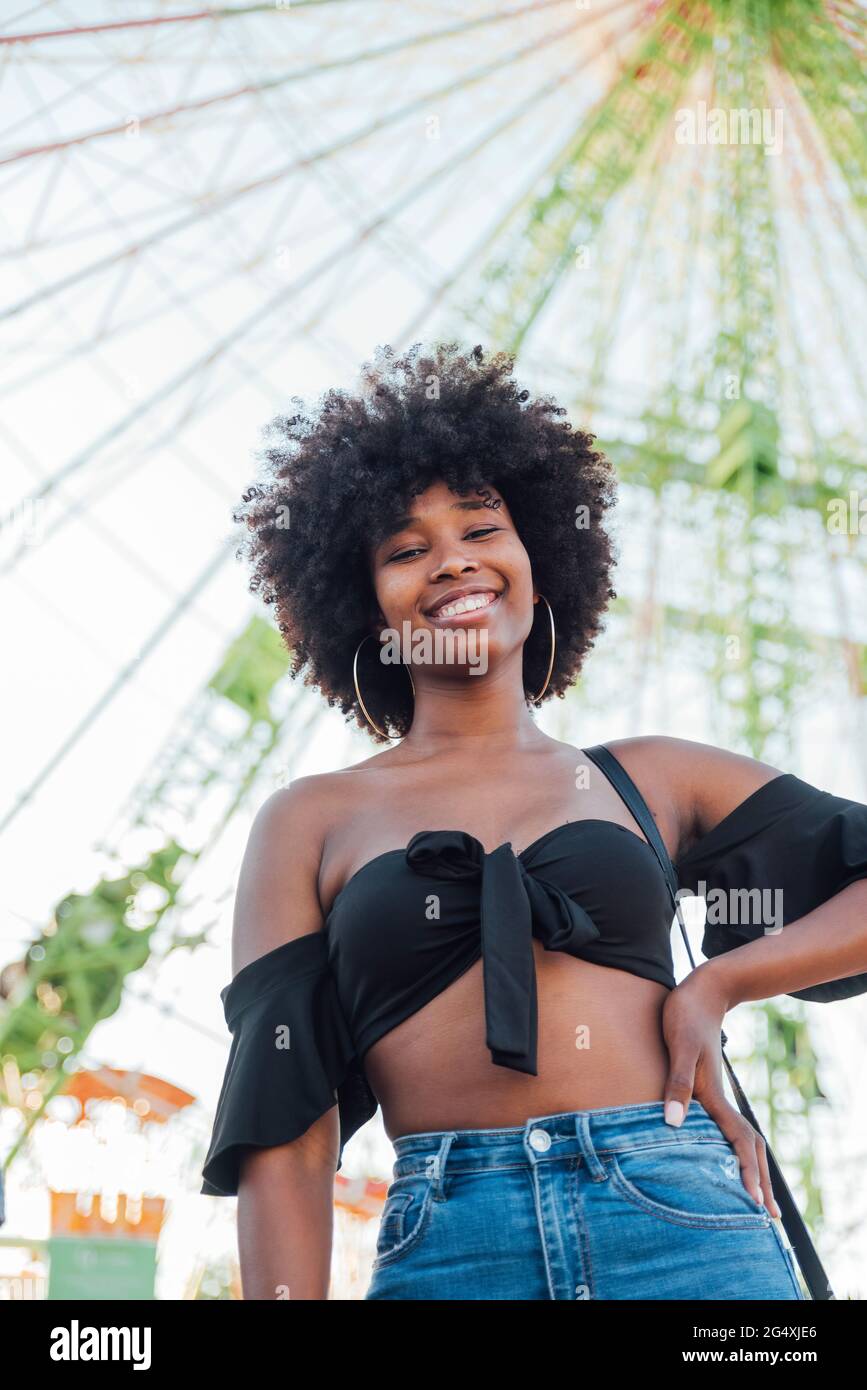 Smiling woman with hand on hip standing in amusement park Stock Photo