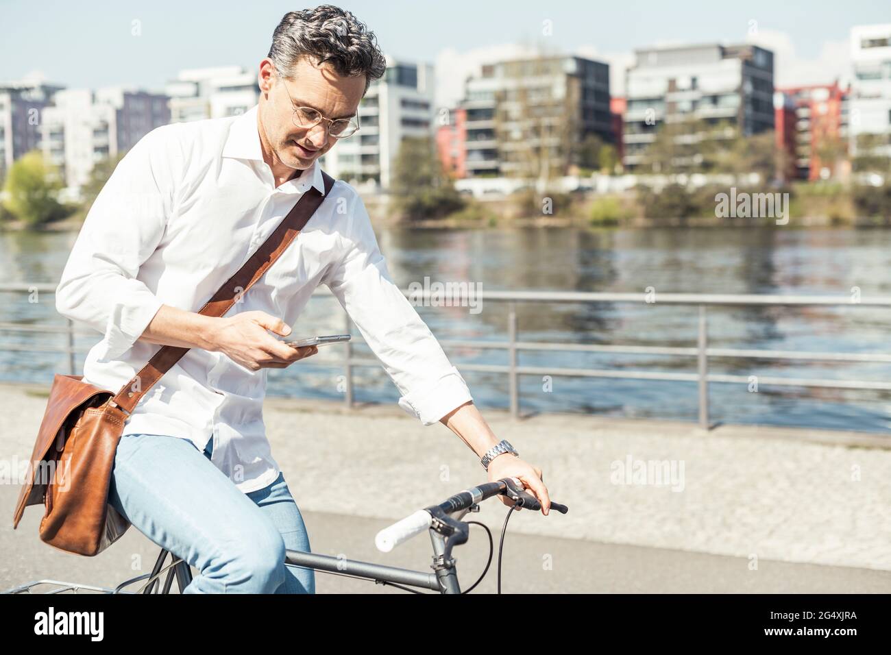 Businessman using mobile phone while cycling bicycle on sunny day Stock Photo