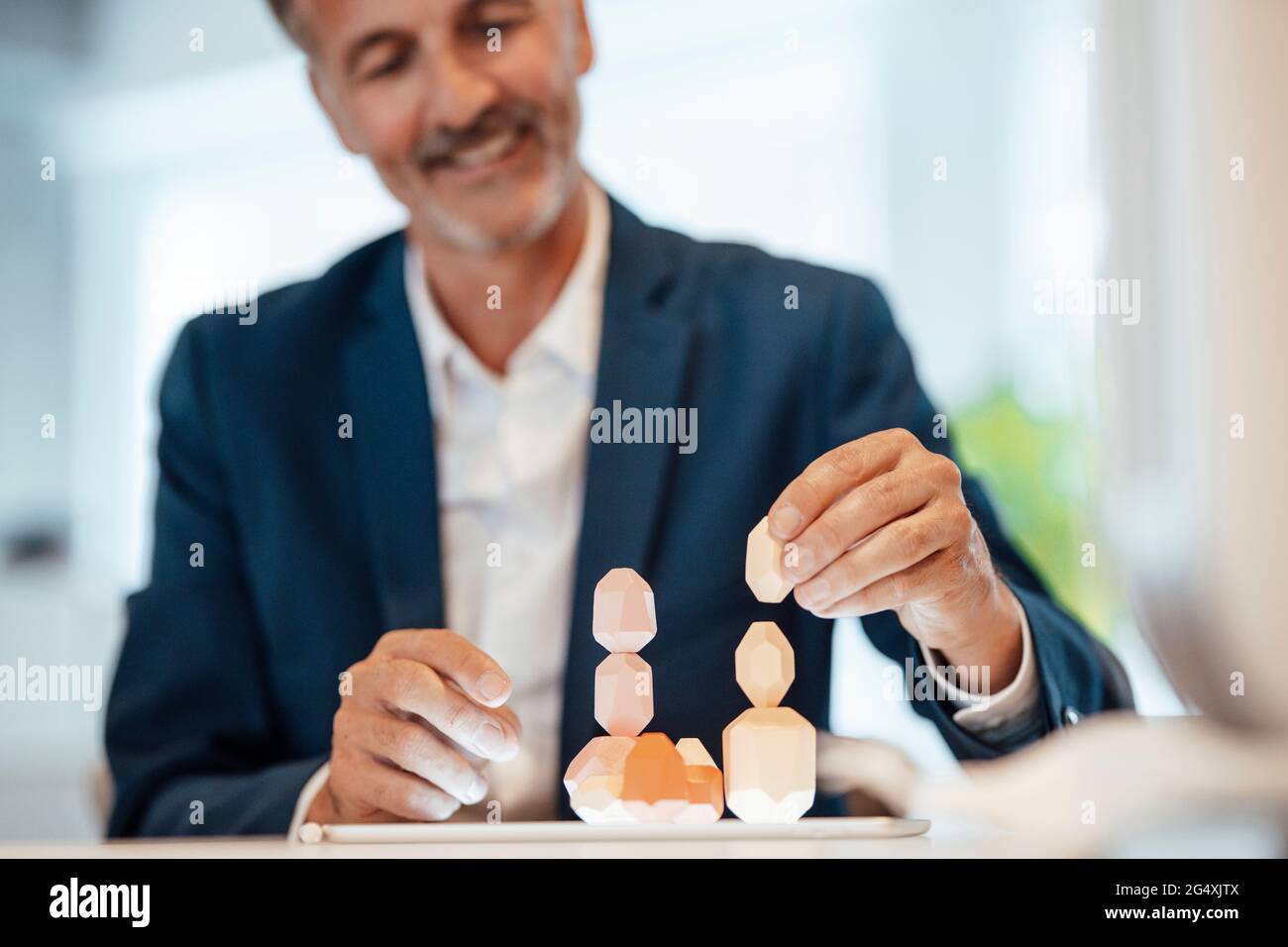 Smiling businessman stacking wooden rock in office Stock Photo