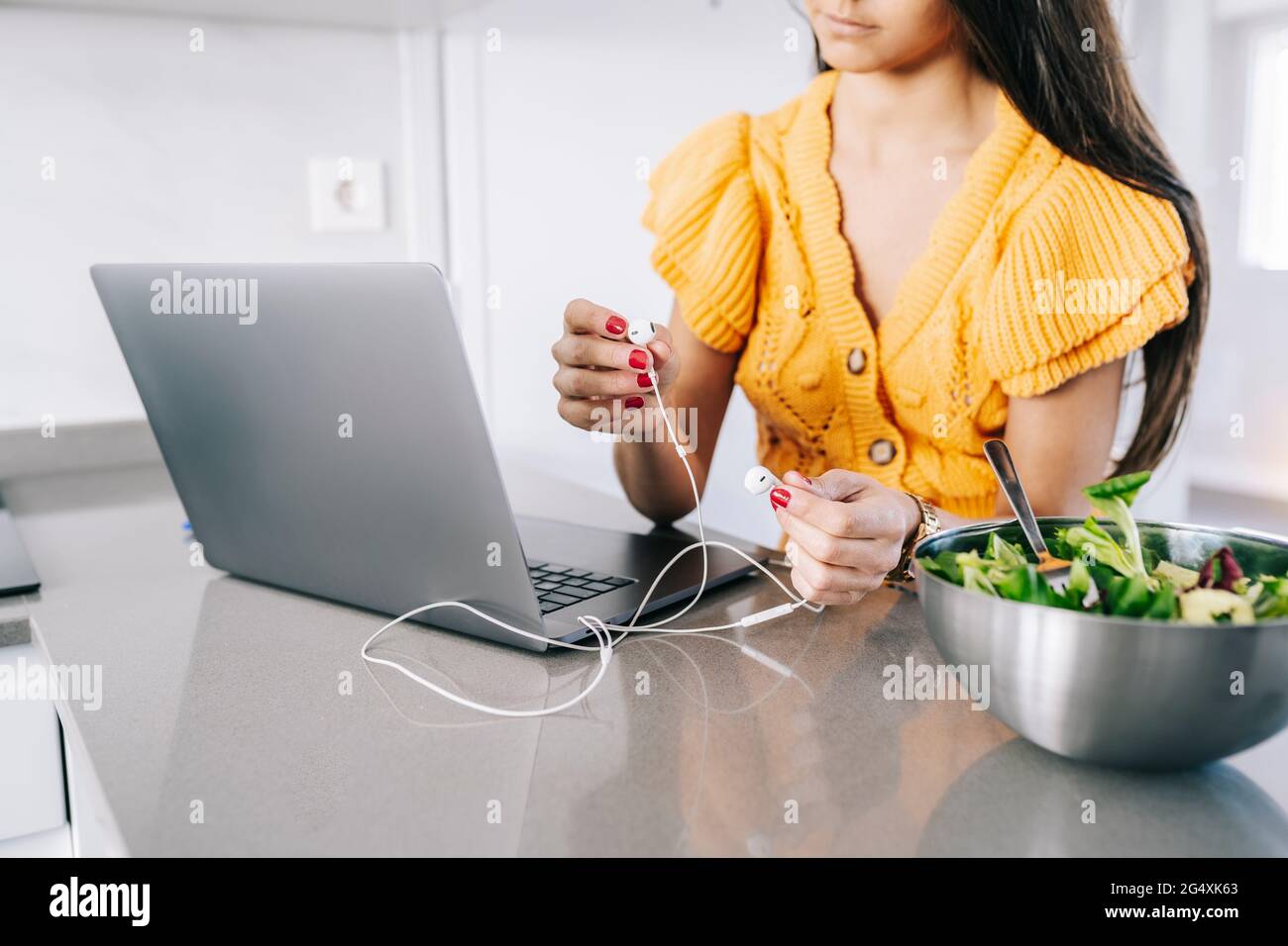 Woman holding in-ear headphones by laptop at home Stock Photo