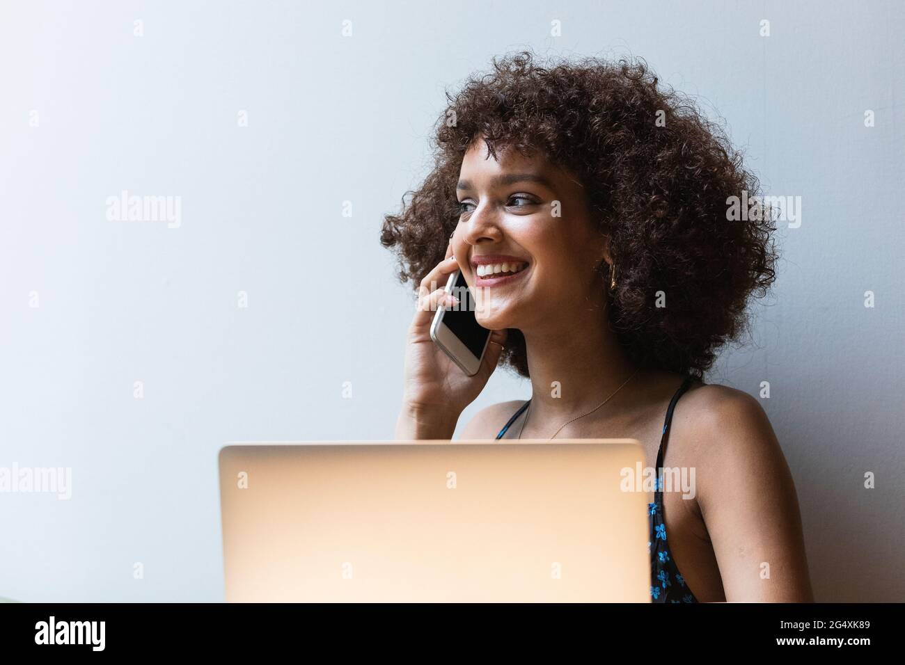 Smiling university student with laptop talking on mobile phone Stock Photo