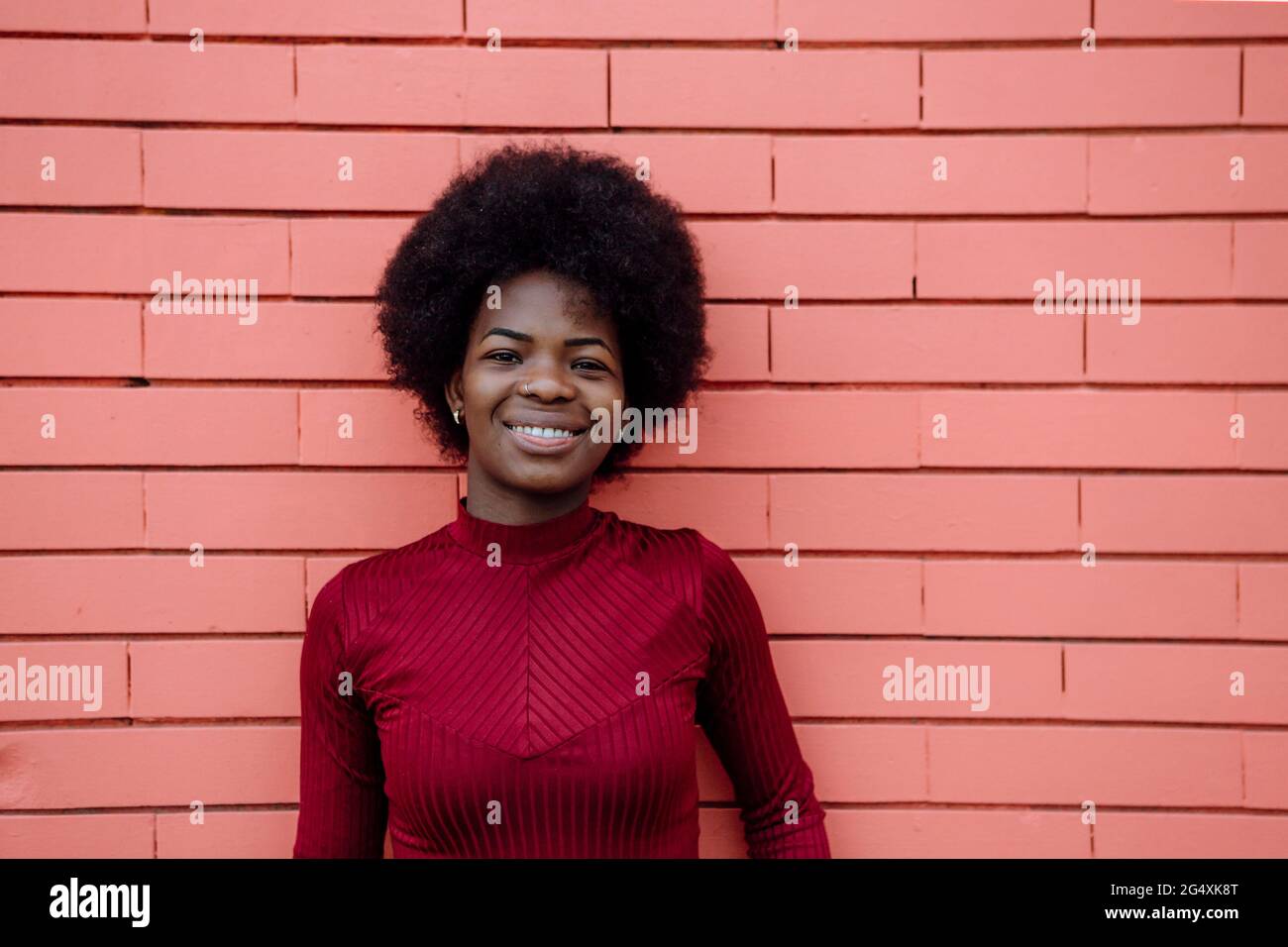 Smiling Afro woman standing in front of brick wall Stock Photo - Alamy