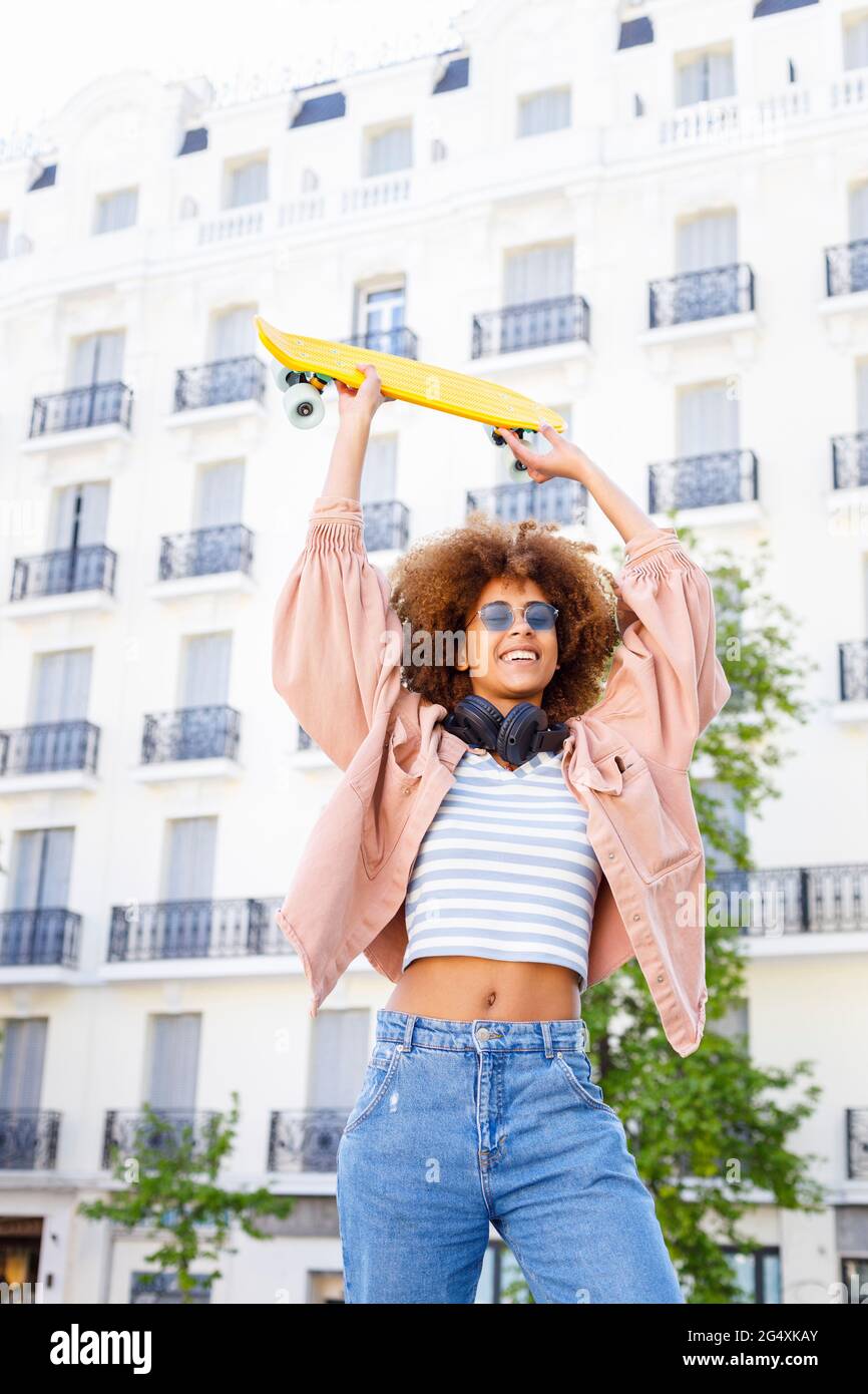 Cheerful young woman looking away while holding yellow skateboard Stock Photo