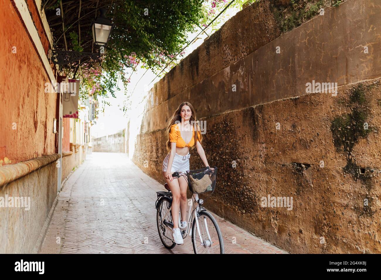 Smiling woman cycling in alley Stock Photo