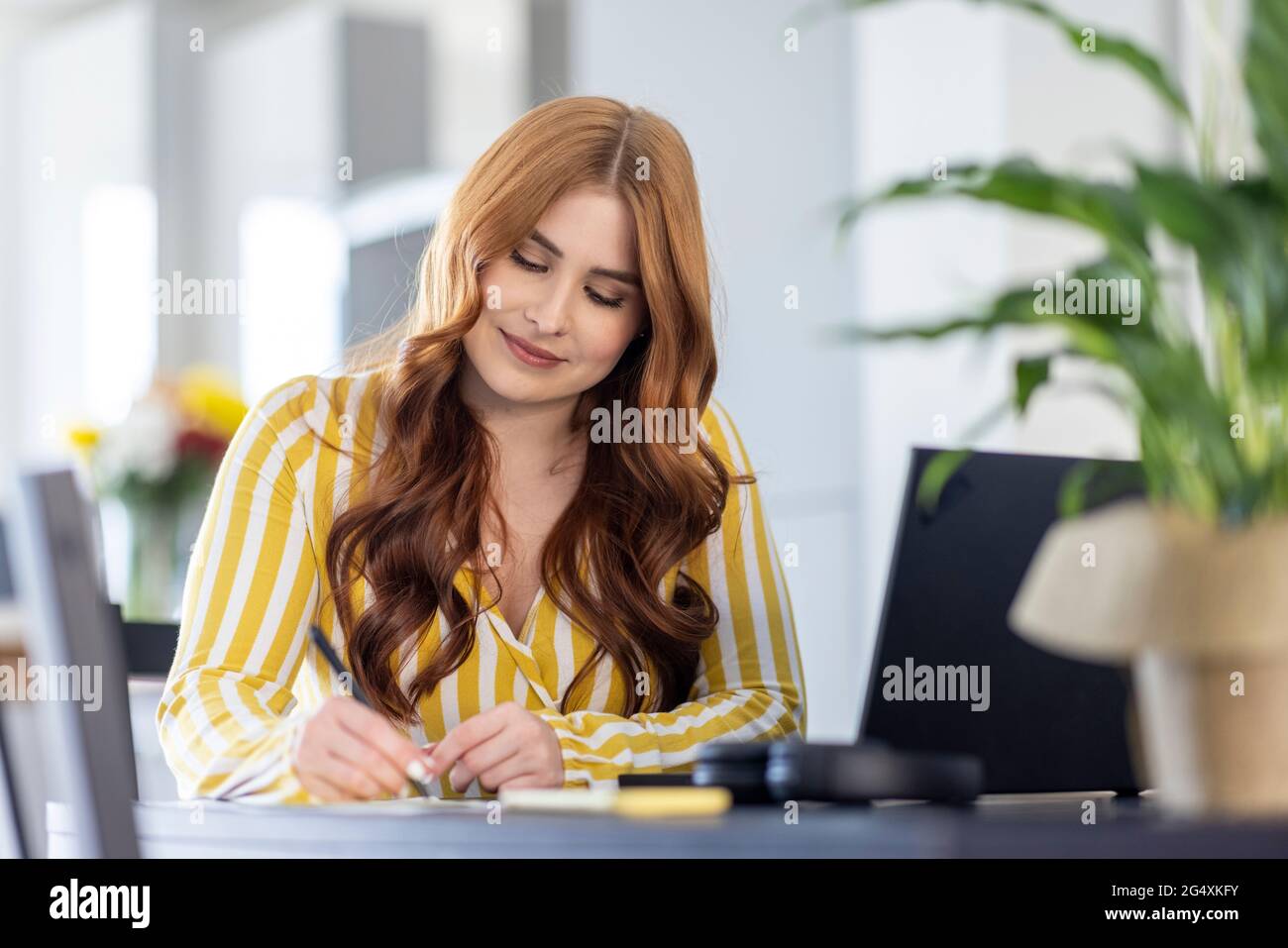 Redhead female freelancer writing while working from home Stock Photo
