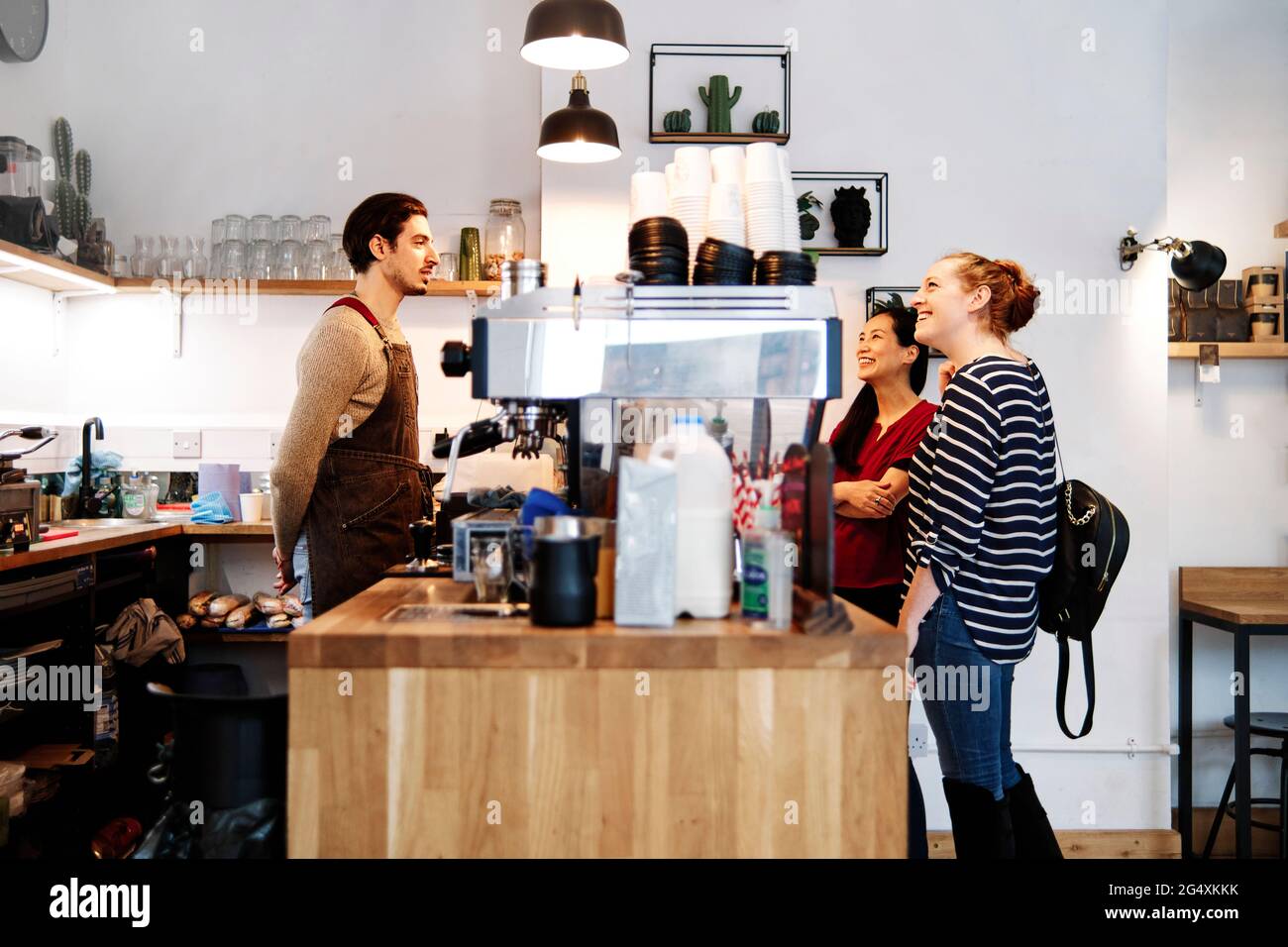 Smiling female customers looking at pendant light while standing in front of owner at coffee shop counter Stock Photo
