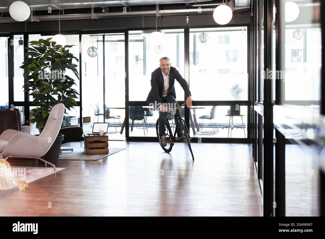 Smiling businessman cycling in office Stock Photo