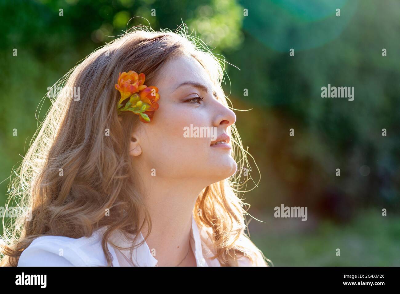 Beautiful young woman with blond hair wearing freesia flower looking away Stock Photo
