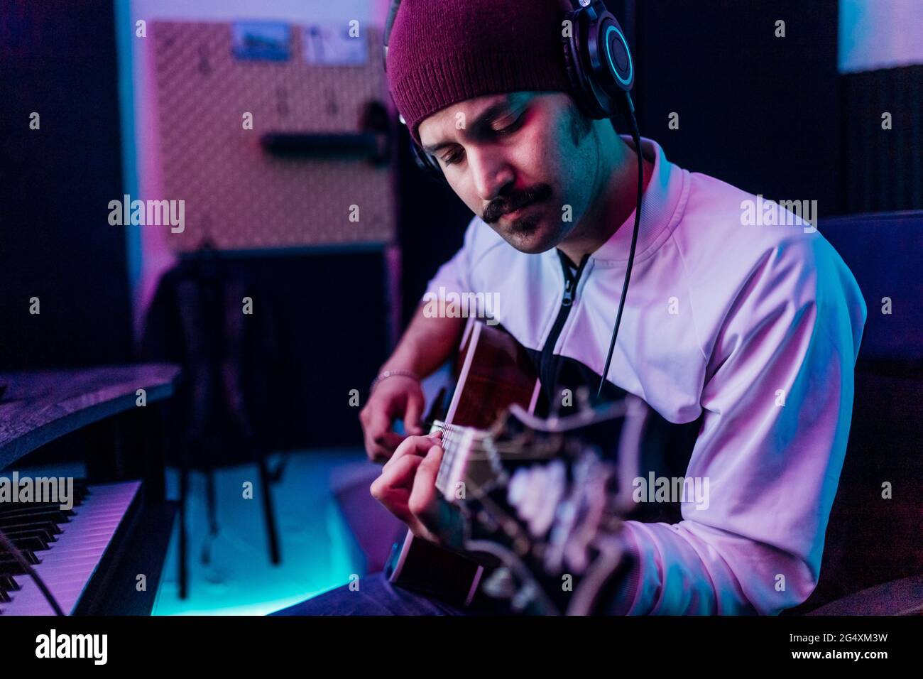 Male guitarist wearing knit hat playing guitar at home studio Stock Photo