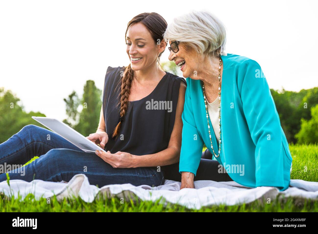 Smiling women using digital tablet while sitting on picnic blanket Stock Photo