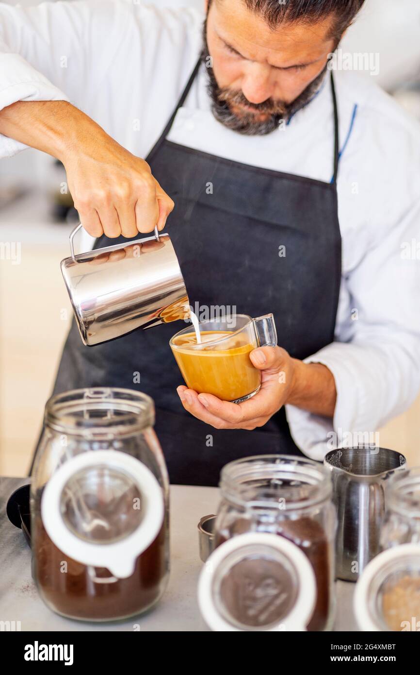 Chef pouring milk while working in commercial kitchen at restaurant Stock Photo