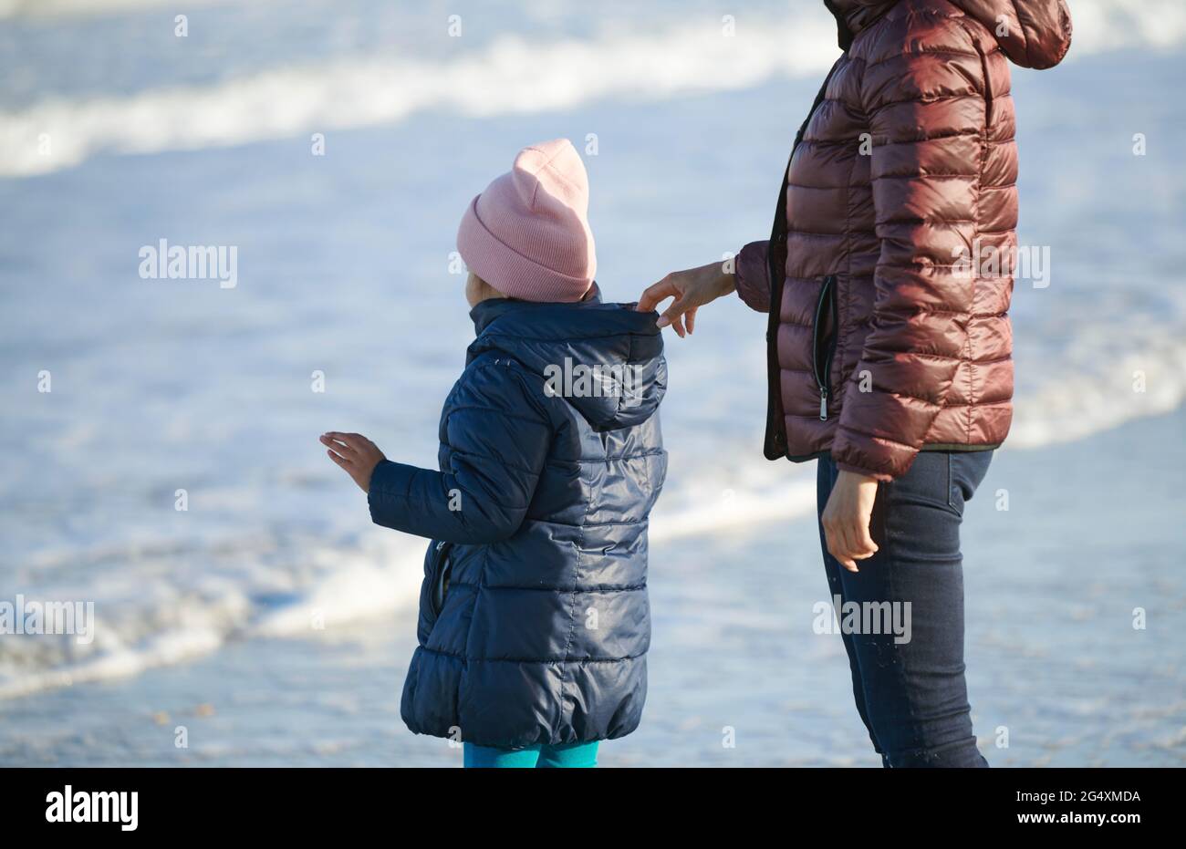 Careful woman holding daughter from hood at beach Stock Photo