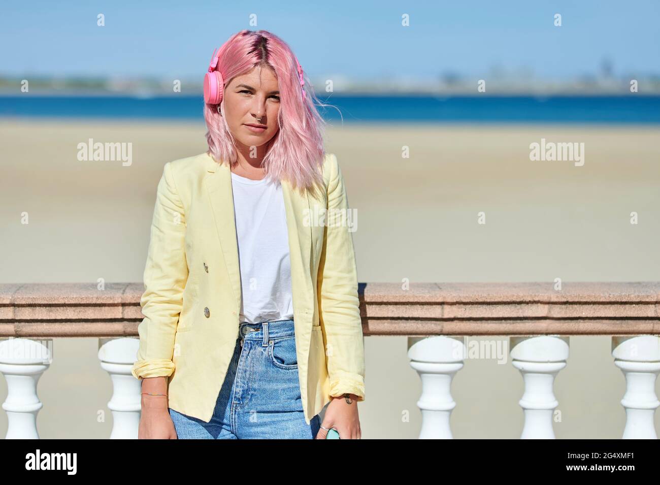 Young woman with pink hair leaning on railing at beach Stock Photo