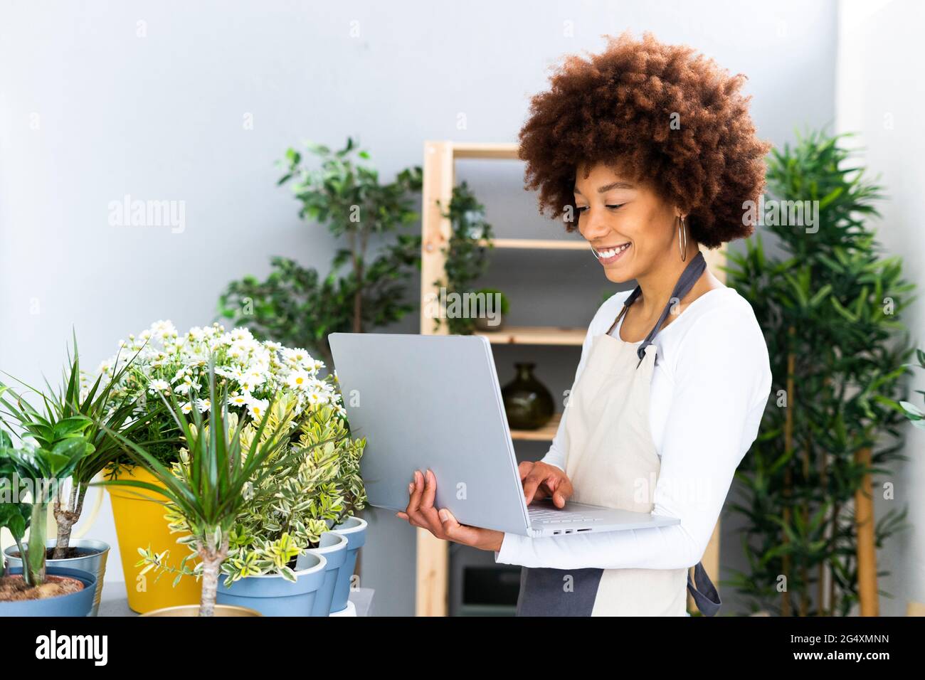 Smiling florist using laptop while standing by plants in shop Stock Photo