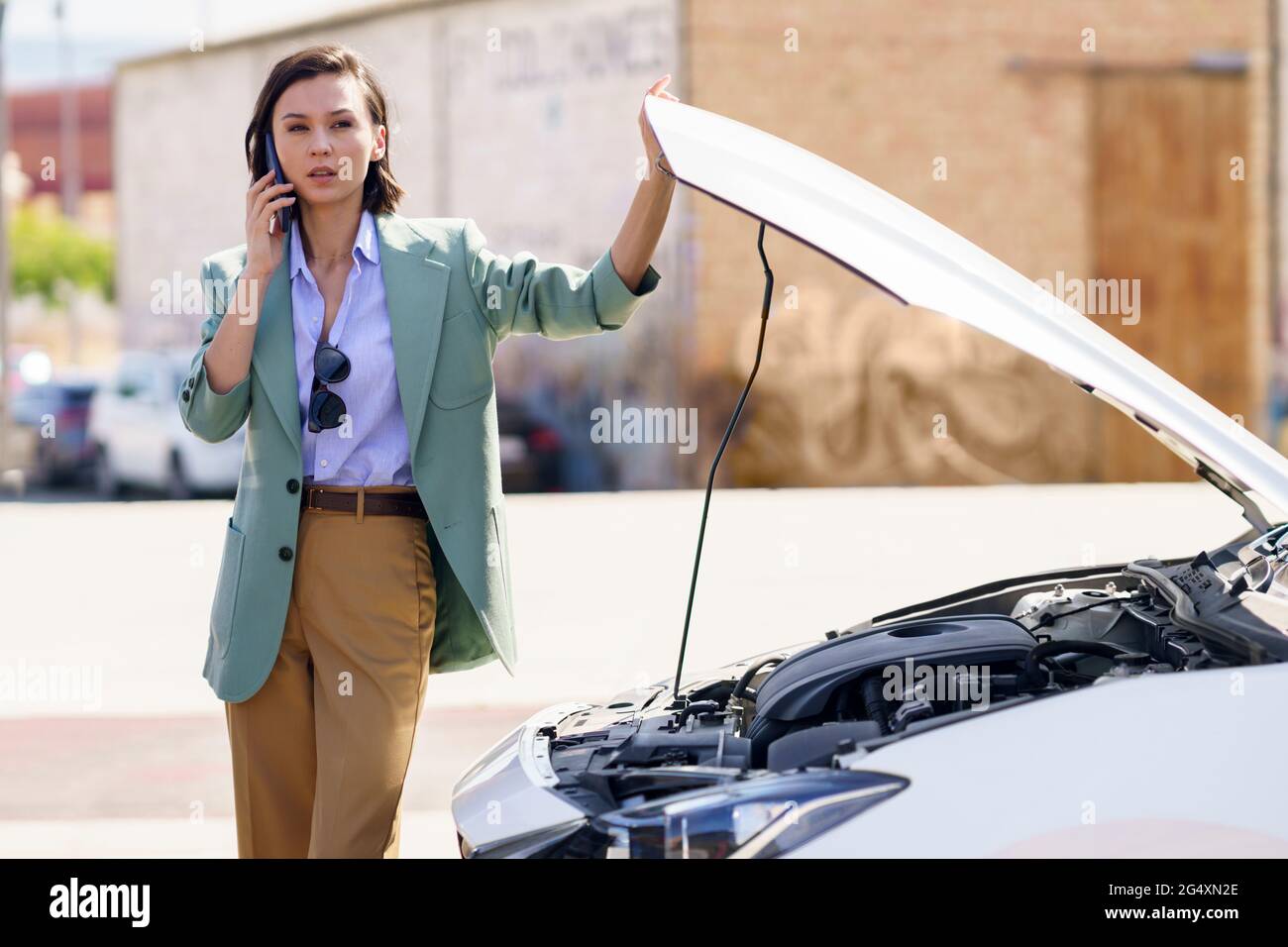 Businesswoman talking on smart phone by broken down car Stock Photo