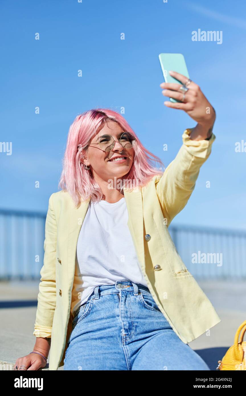 Pink haired woman taking selfie through mobile phone at promenade Stock Photo