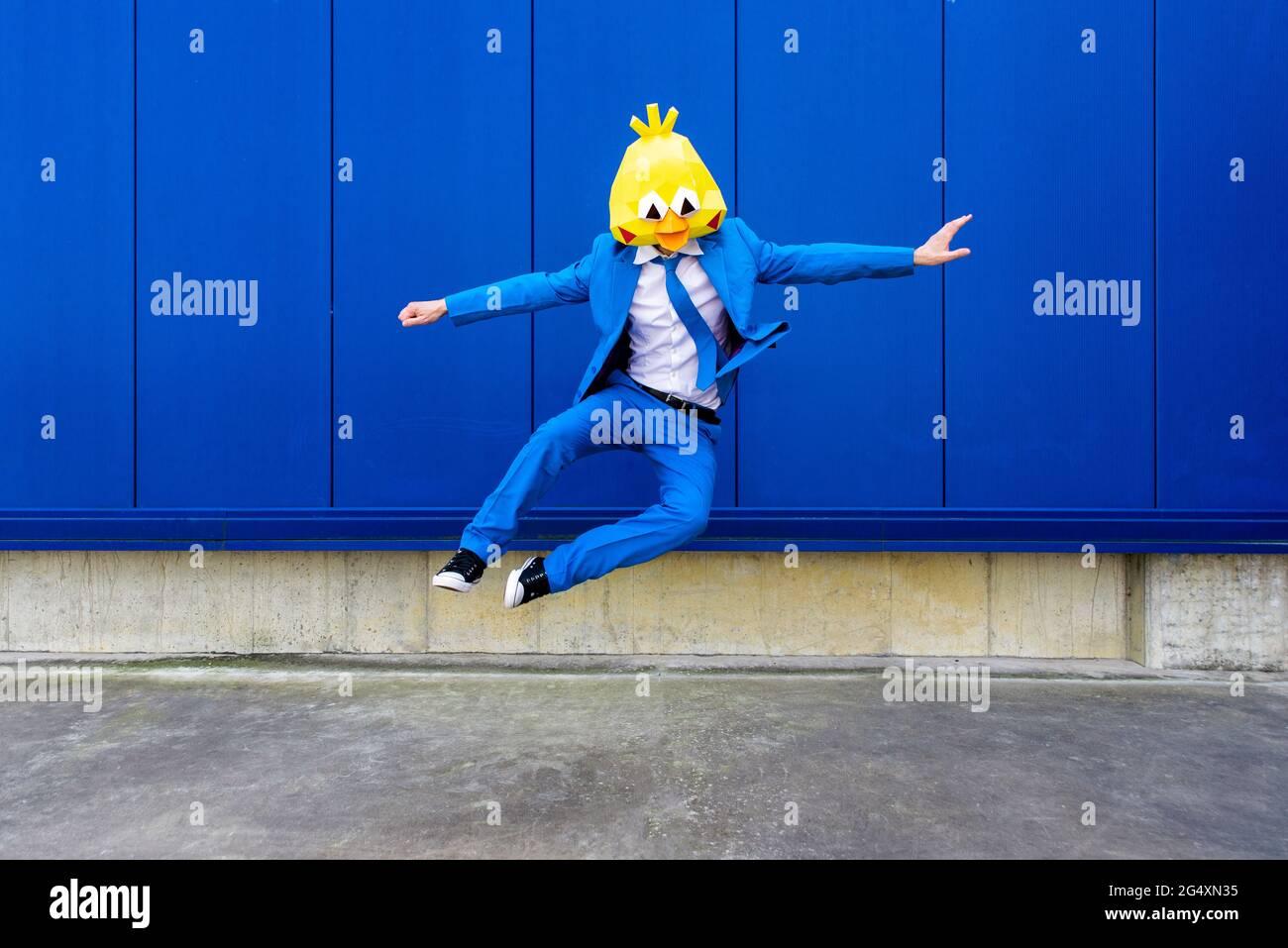 Man wearing vibrant blue suit and bird mask jumping against blue wall