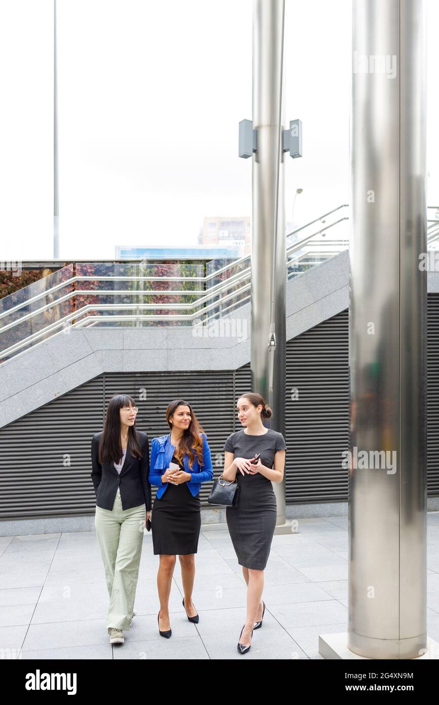 Female colleagues discussing while walking on footpath Stock Photo