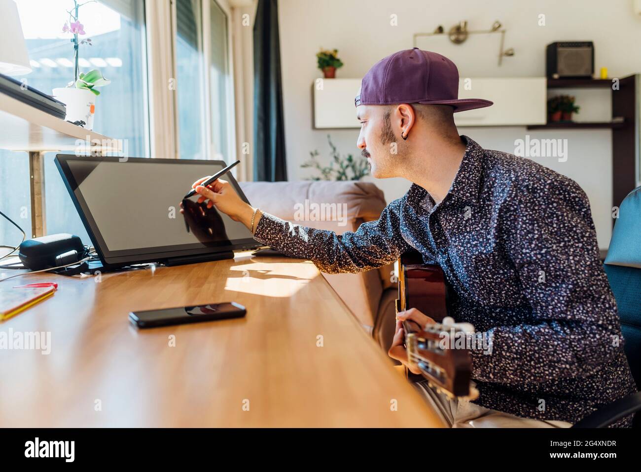 Young male composer with guitar using graphics tablet at home Stock Photo