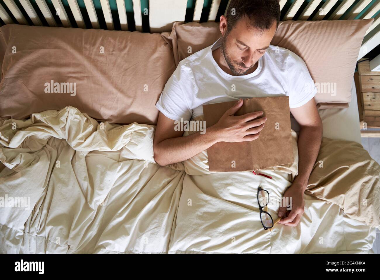 Man with book and eyeglasses napping in bed at home Stock Photo