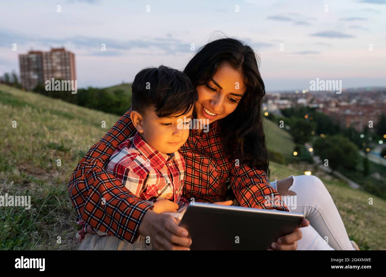 Smiling mother and son using digital tablet while sitting on hill Stock Photo