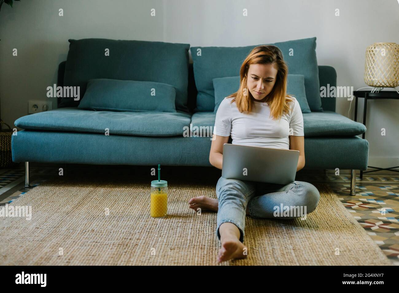 Redhead woman using laptop while sitting on carpet at home Stock Photo ...