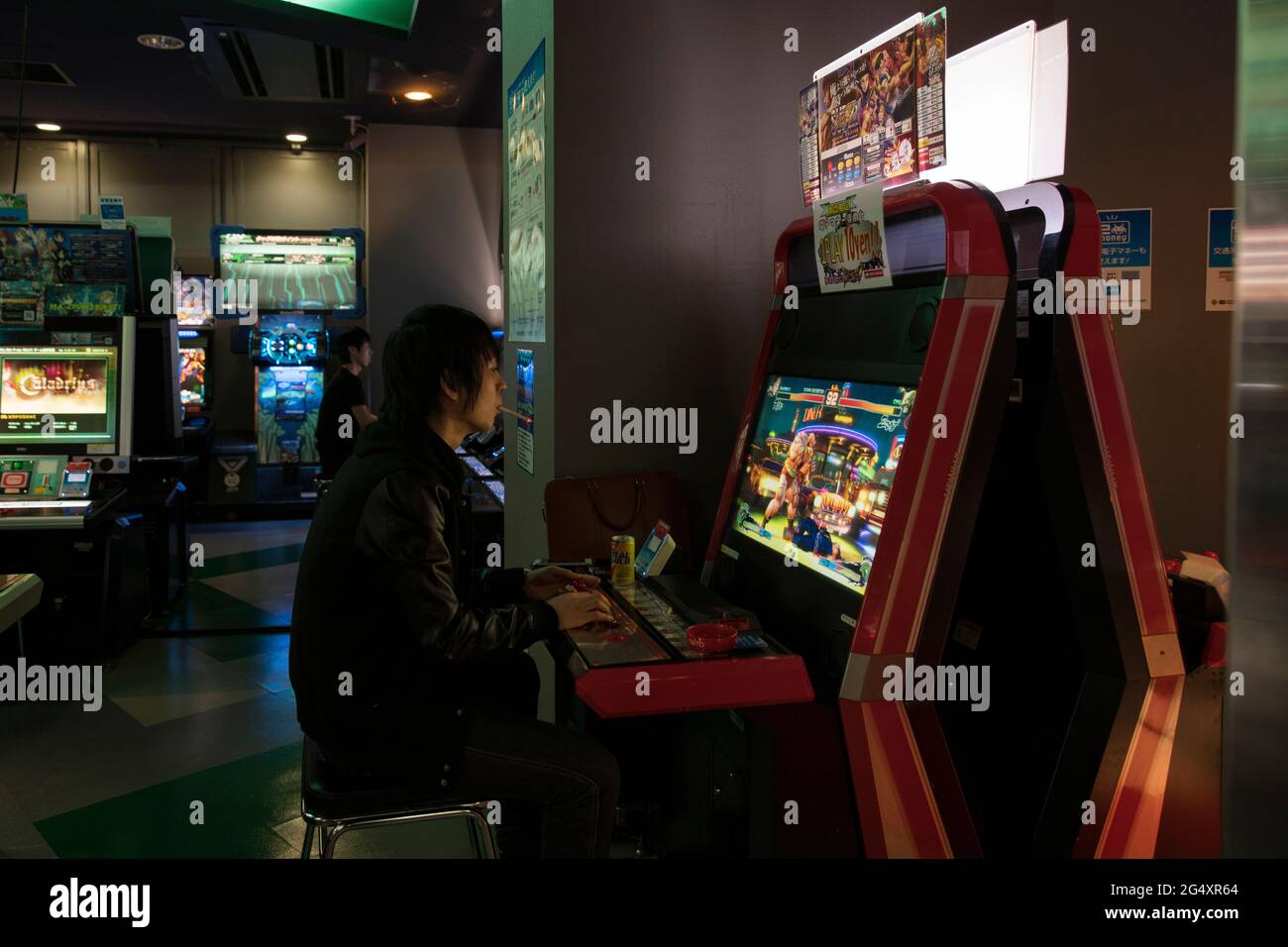 A person smoking while playing videogames in a Japanese arcade Stock Photo