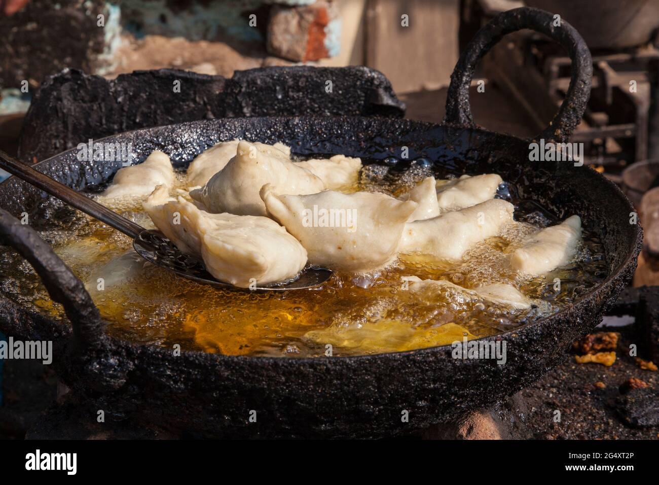 Samosas frying in oil using a traditional karahi at a street vendor's