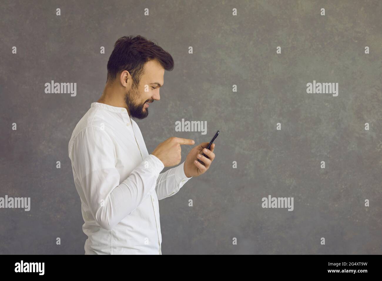 Side view of happy man using mobile phone standing isolated on grey copy space background Stock Photo