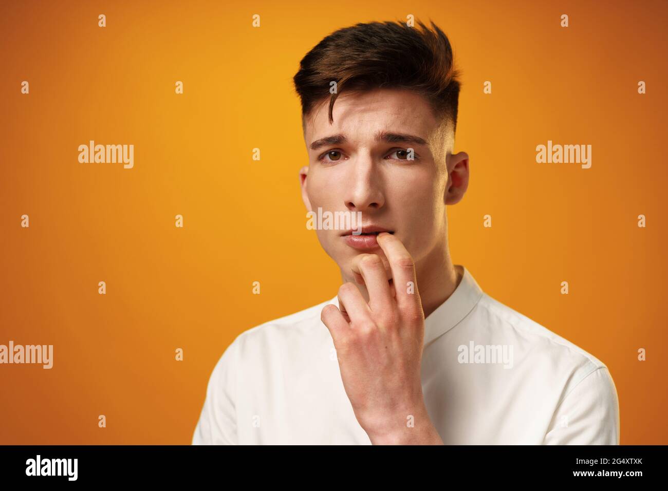 Frustrated and nervous young man biting nail against yellow background Stock Photo
