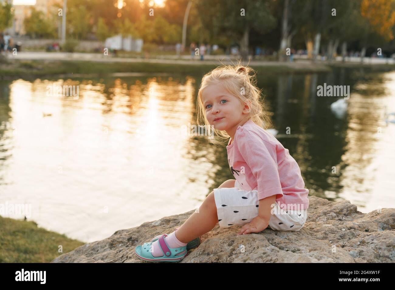 Little girl sitting on a huge stone in park near the lake Stock Photo ...