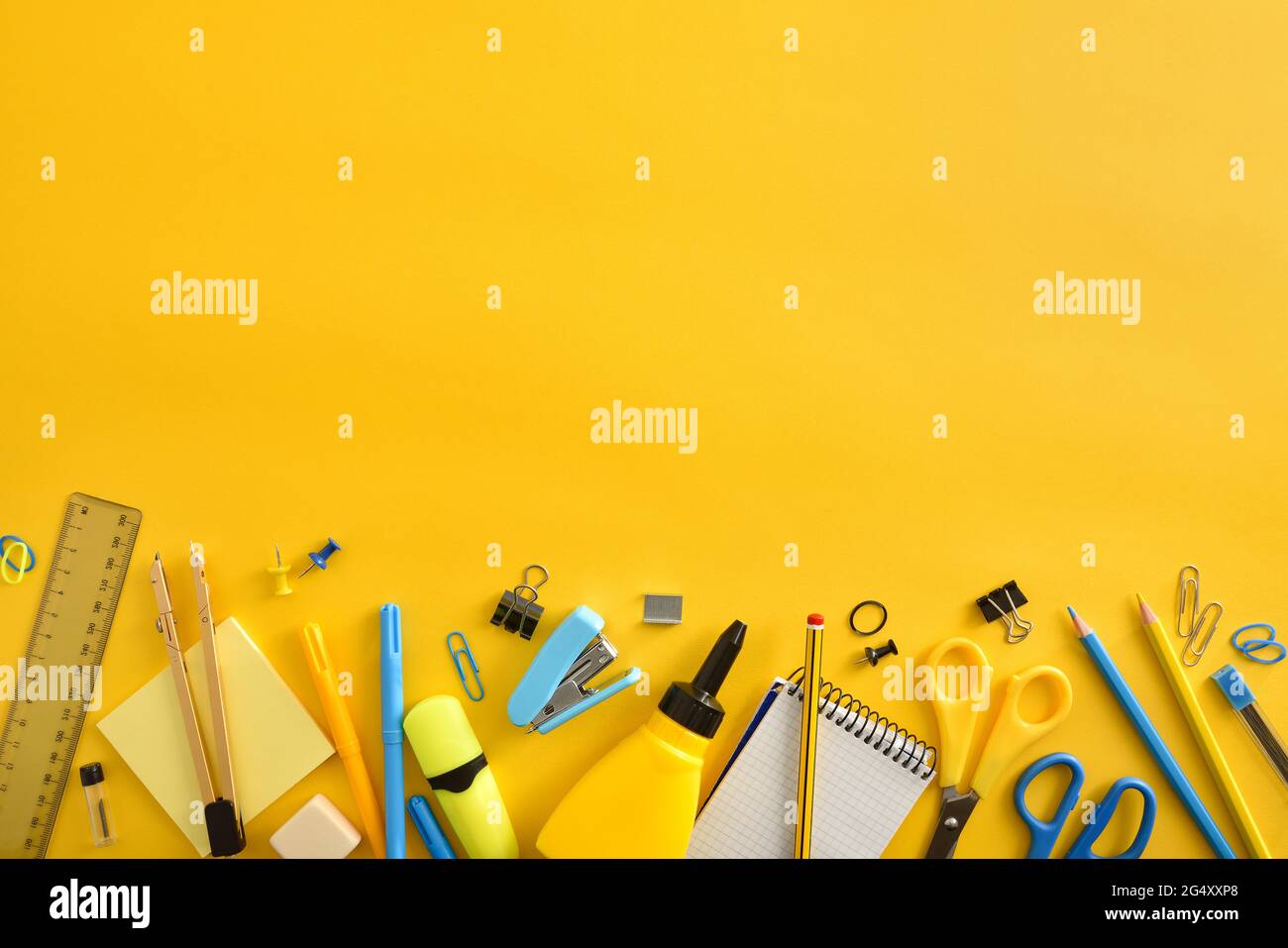 Row of yellow and blue school supplies on yellow background and top