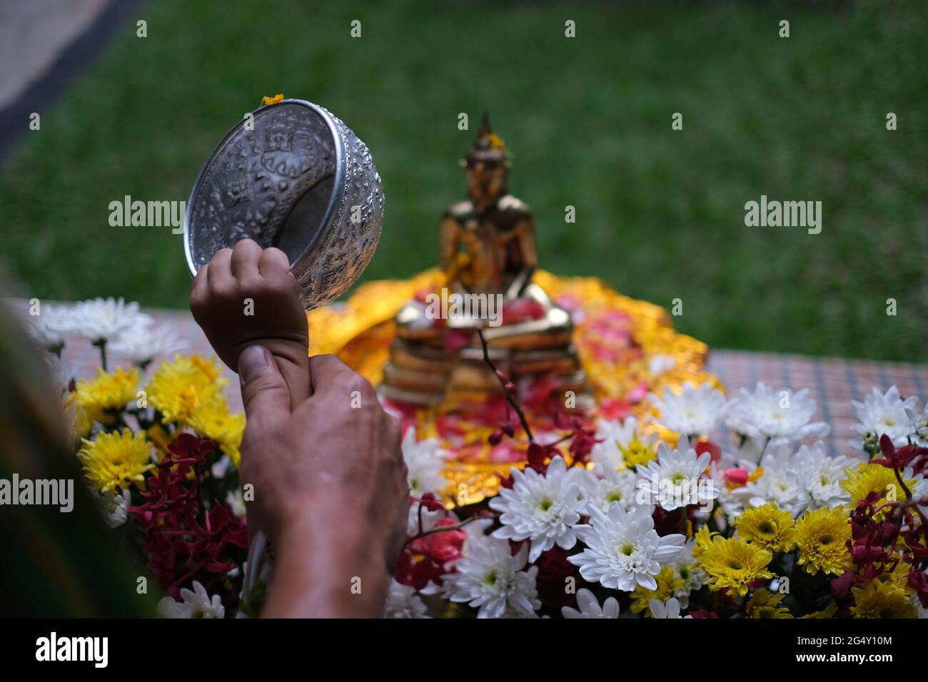Hands of father and son, while father is teaching sibling how to pour water with silver bowl to bronze Buddha's statue at Songkran Day Stock Photo