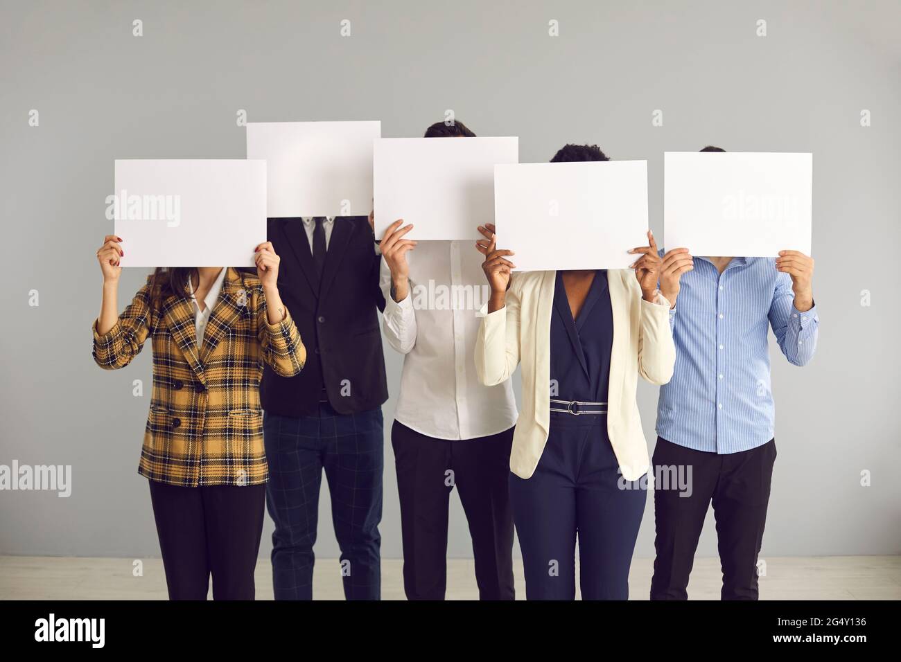 Group of anonymous people covering faces hiding behind white mockup sheets of paper Stock Photo