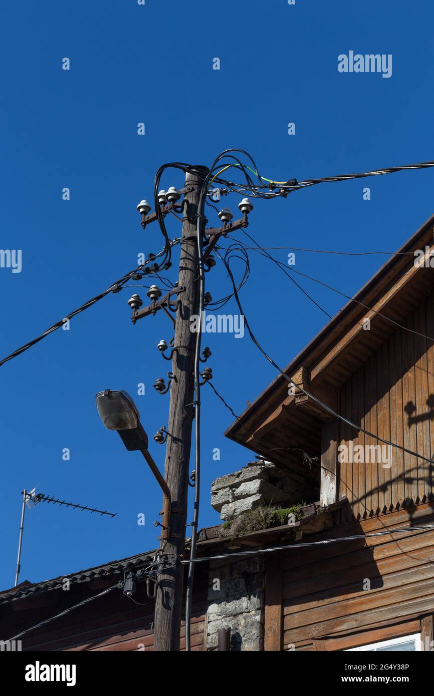 old wires on electric pole over blue sky and old house Stock Photo