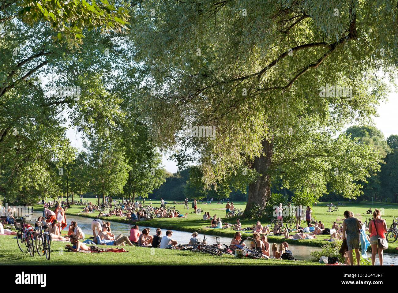 Munich - Bayen- Germany, June 11th, 2021: People who relax in the grass and do sports like cycling on the EIsbach. At the weekend, many went to the En Stock Photo