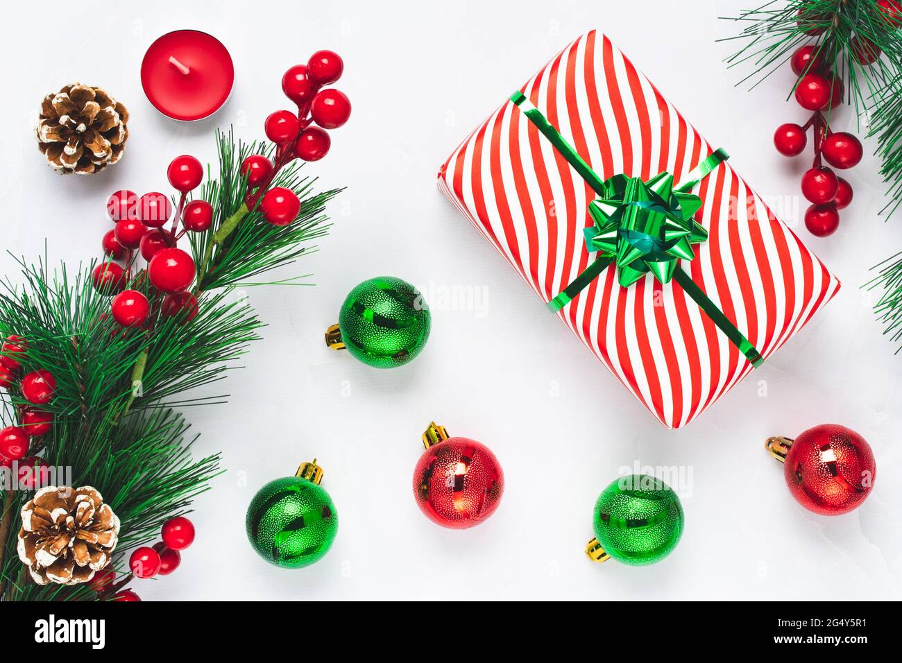 Christmas tree with New Year decorations on white background. Celebration card with gift box and fir branches with red holly berry Stock Photo