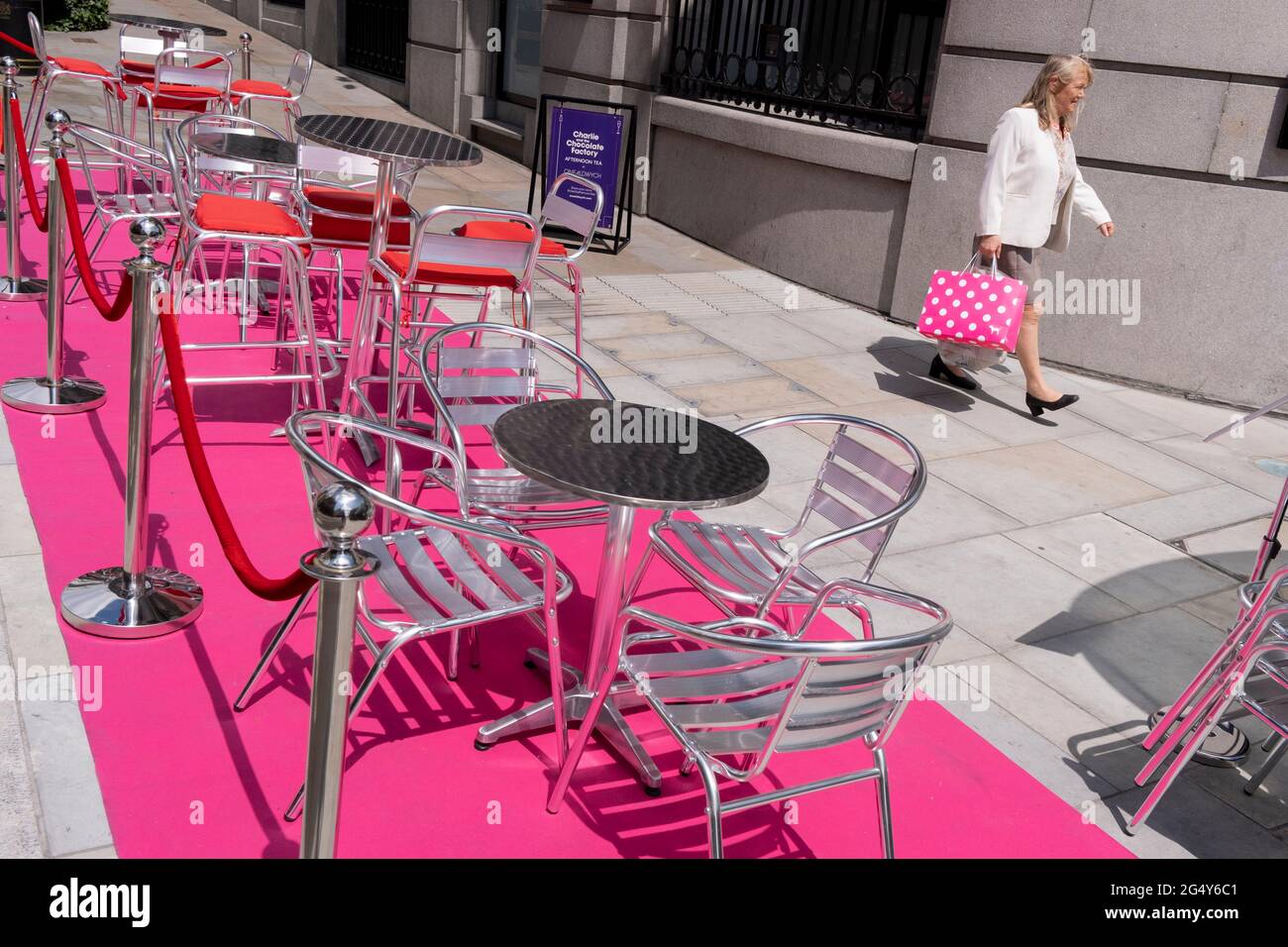 A woman carries a pink shopping bag past a pink carpet with silver