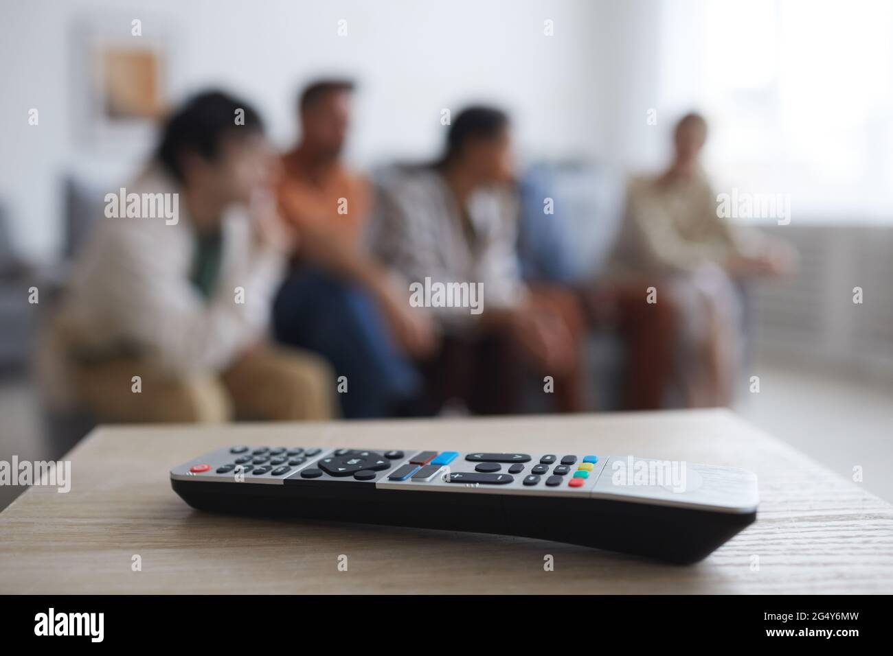 Close up of TV remote on table with blurred group of people watching movies at home in background, copy space Stock Photo