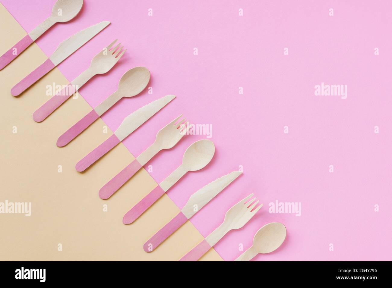 Disposable bamboo spoons, forks and knives on yellow and pink