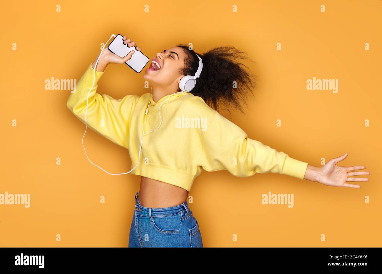 Cheerful girl listens favorite song in headphones, sings words on yellow background Stock Photo