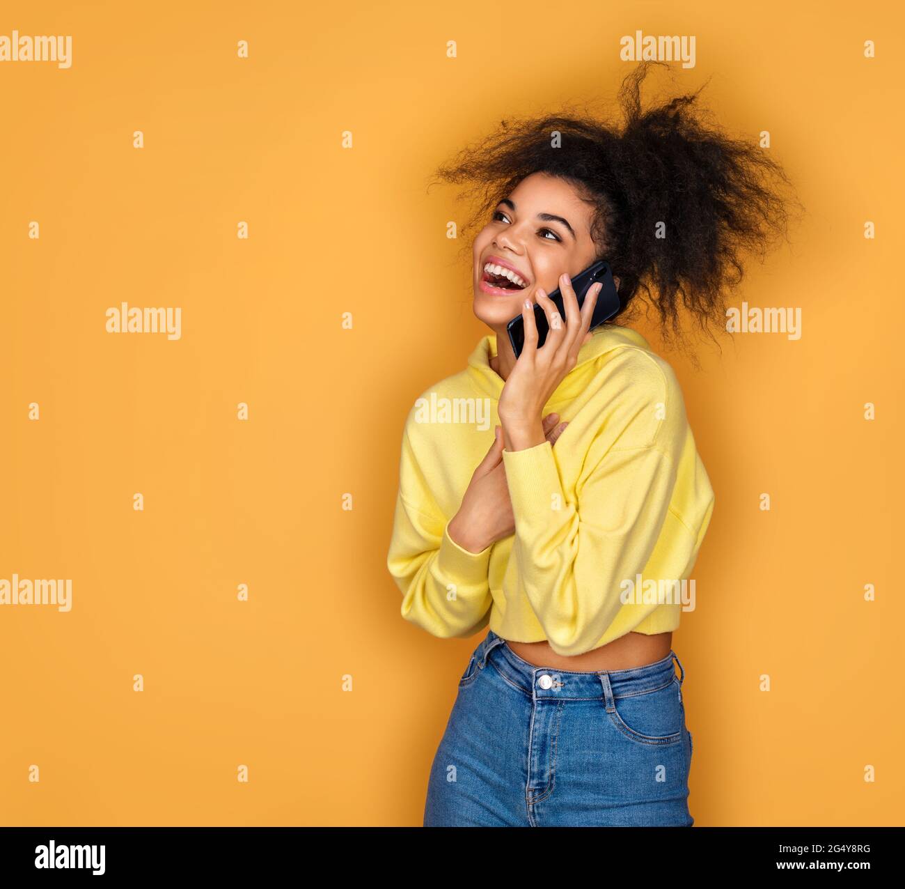 Girl is talking on the phone and smiling. Photo of african american girl on yellow background Stock Photo