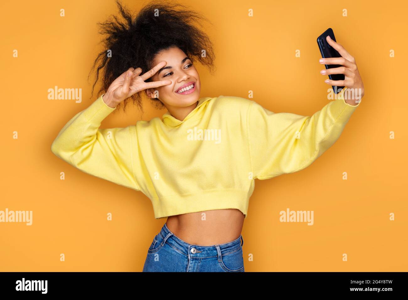 Young girl holds smartphone and takes selfie photo, smiles at camera. Photo  of african american girl on yellow background Stock Photo - Alamy, image size:1300x956