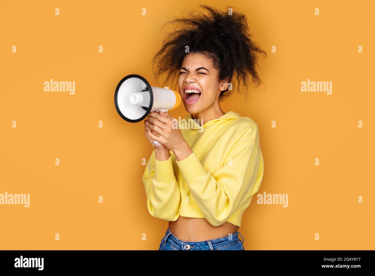 Girl shouts in megaphone. Photo of african american girl on yellow background Stock Photo