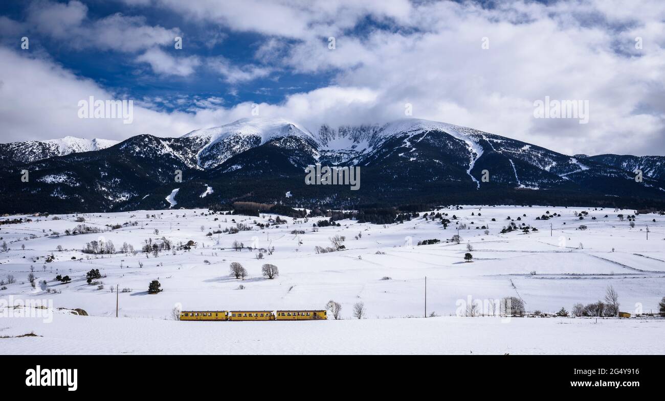 Cambredase peak snowy viewed from Mont-Louis village in a winter afternoon with the Train Jaune (Yellow Train) passing (Pyrenees Orientales, France) Stock Photo