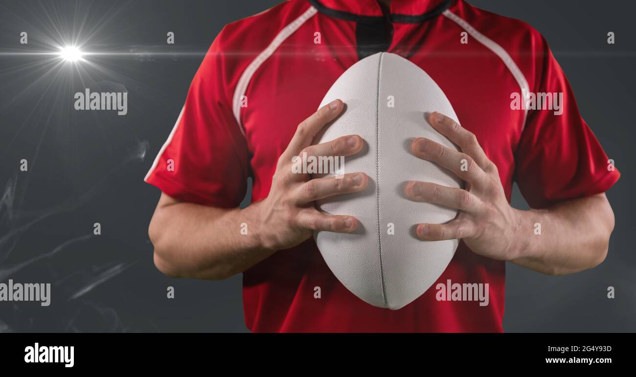 Mid section of male rugby player holding ball against smoke and light spot on grey background Stock Photo